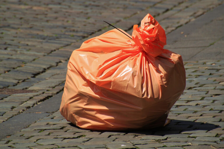 orangener Müllsack liegt auf Boden mit Pflastersteinen