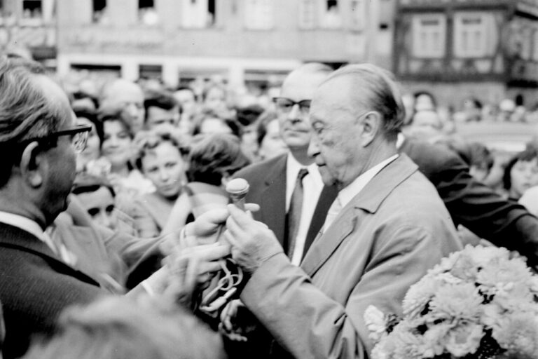 schwarz-weis Foto von einem Mann mit einem Mikrofon in der Hand, viele Personen versammeln sich um ihn herum