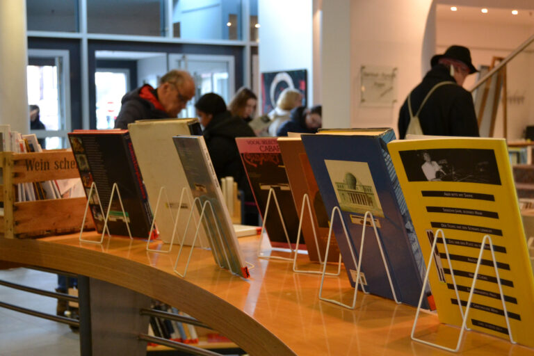 viele aufgestellte Bücher mit Personen im Hintergrund