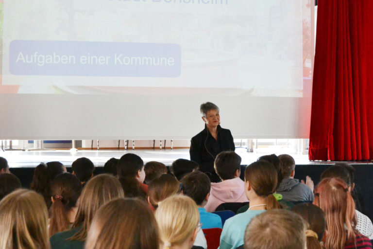 viele sitzende Personen, eine Stehende vor Leinwand