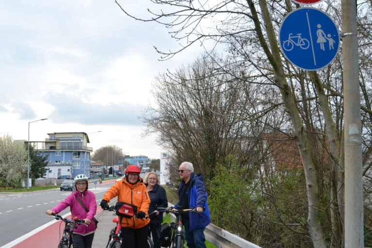 Straßenschild, vier Fahrradfahrende neben der Straße