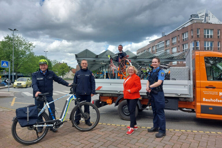 vier Personen lächelnd vor Lastwagen, vor zwei Personen steht ein Fahrrad
