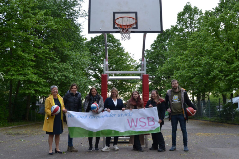 viele Personen halten ein Plakat, sie stehen vor einem Basketballkorb