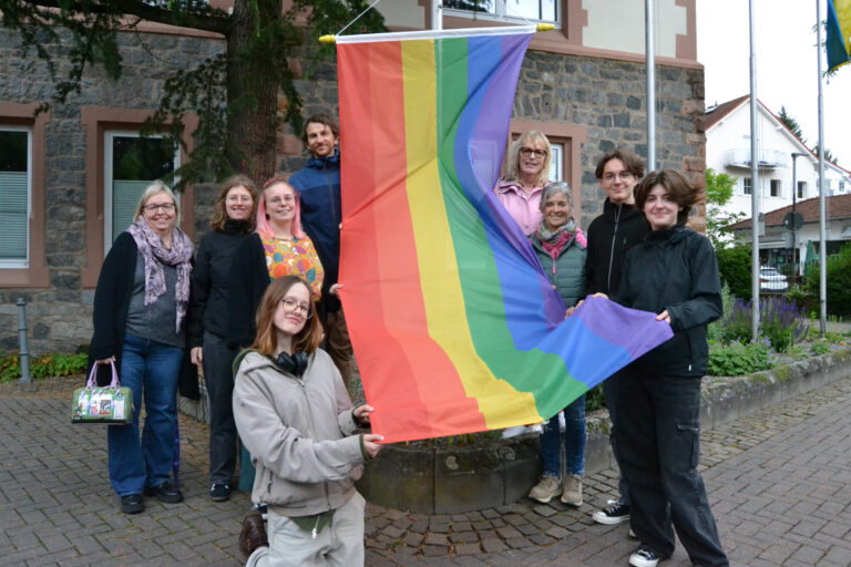 viele Personen halten lächelnd eine Regenbogenfahne