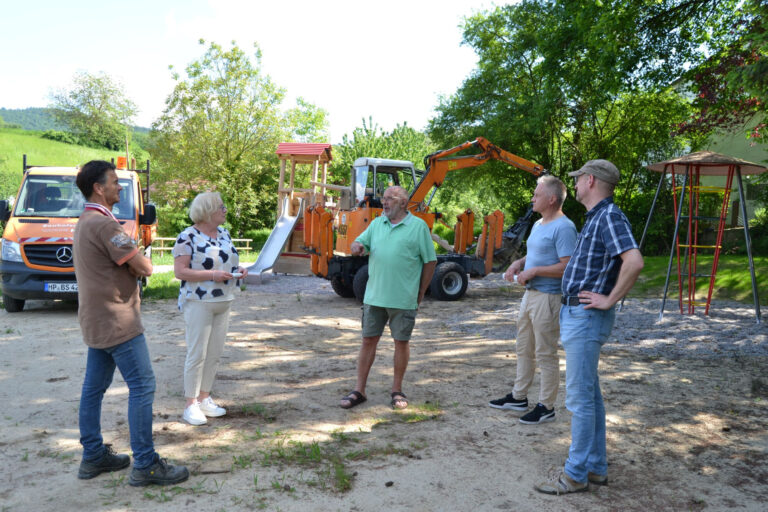 fünf Personen stehen im Kreis, Natur und ein Spielplatz im Hintergrund