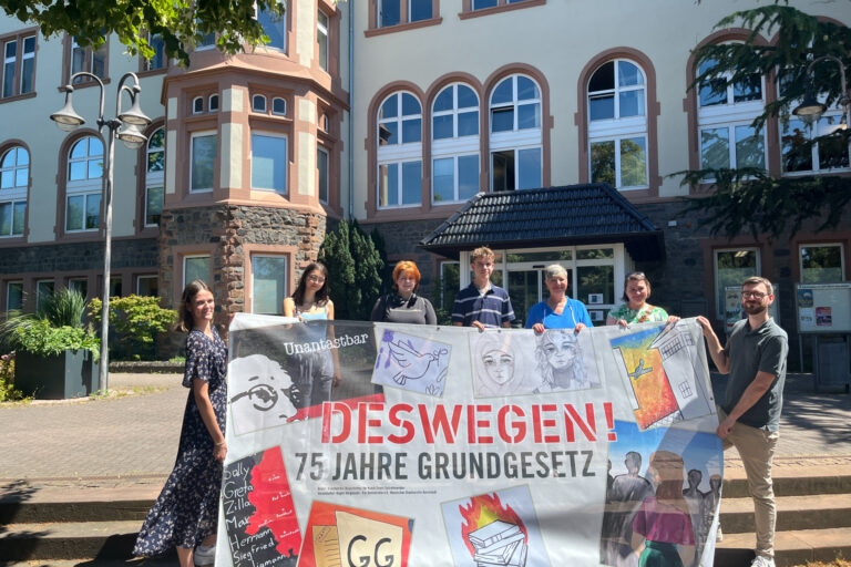 mehrere Personen halten ein Plakat vor einem Gebäude