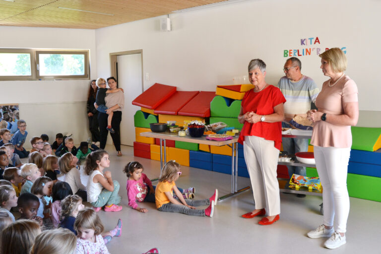 viele kleine Kinder schauen zu zwei Frauen, die vor einem Buffet stehen
