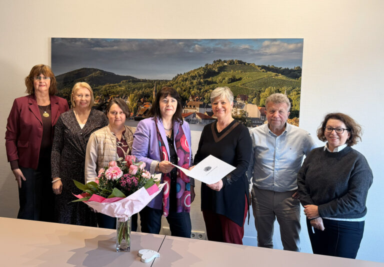 Personen stehend vor Bild mit Blumen und Urkunde in der Hand