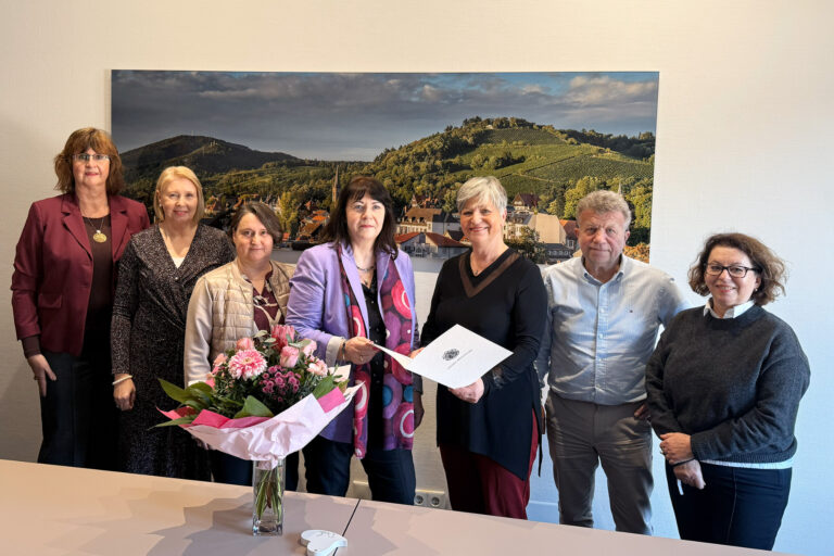 Personen stehend vor Bild mit Blumen und Urkunde in der Hand