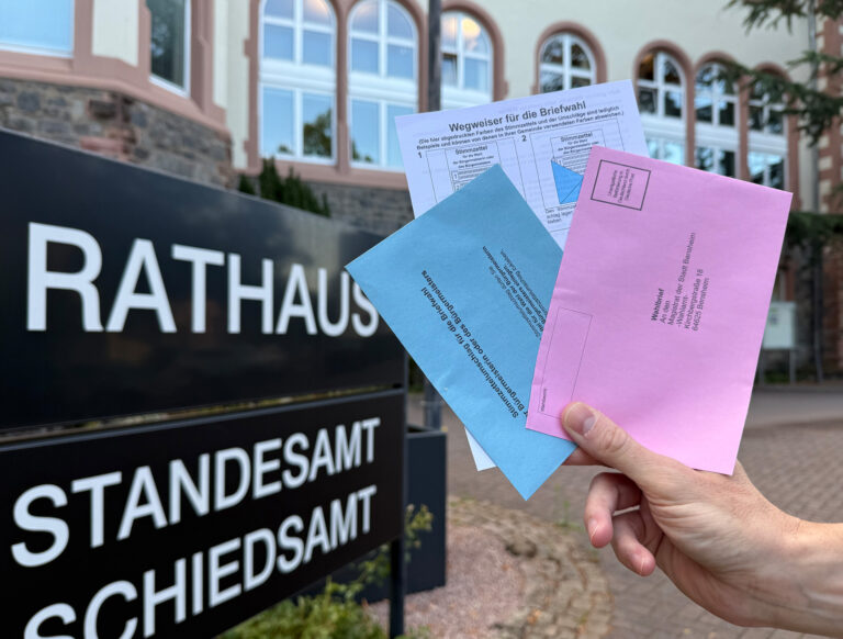 Briefwahlunterlangen im Vordergrund und dahinter das Rathaus
