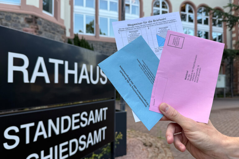 Briefwahlunterlangen im Vordergrund und dahinter das Rathaus