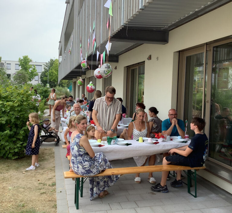 Personen sitzend und stehend an Tischen und feiern