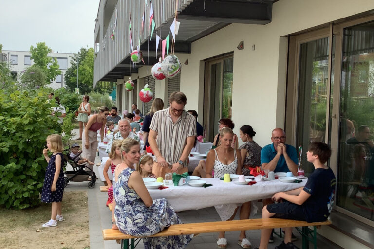 Personen sitzend und stehend an Tischen und feiern