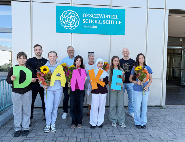 Personen stehend mit Buchstaben und Blumen in der Hand vor einem Gebäude